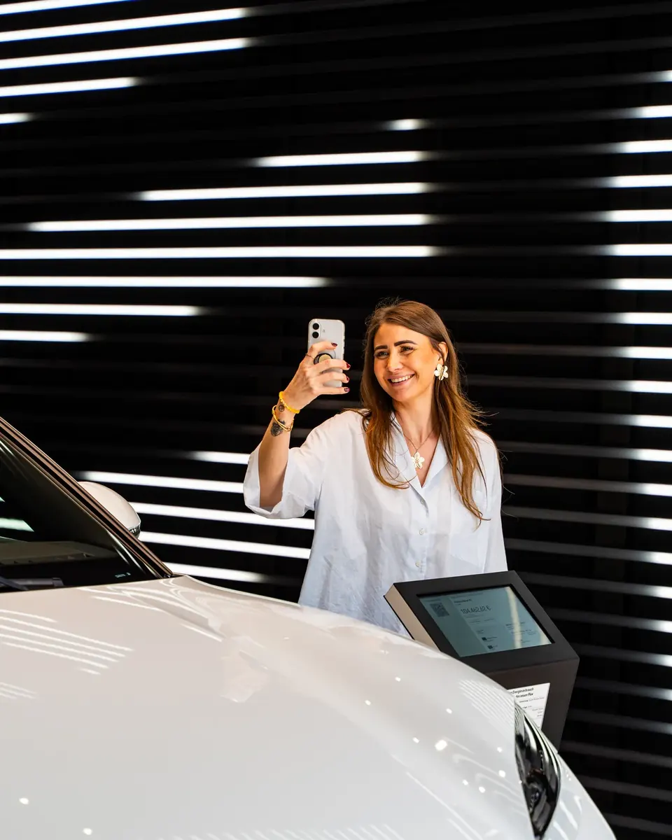 Teammitglied filmt mit dem Smartphone einen weißen Porsche im Showroom