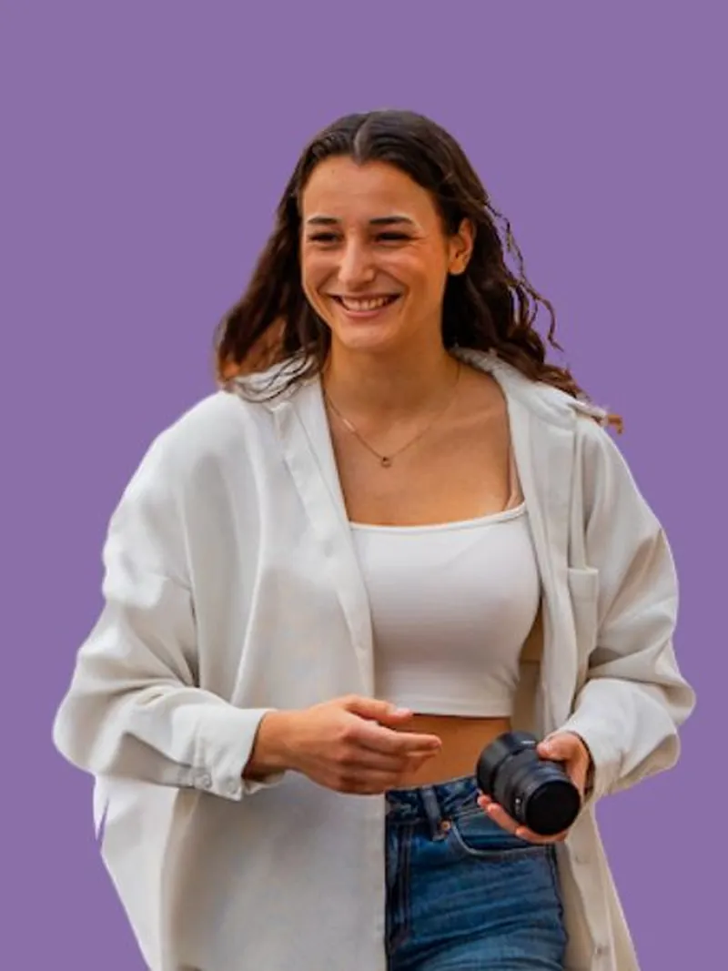 Alisha lacht mit Kamera in der Hand vor violettem Hintergrund